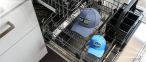 A dishwasher with two baseball caps presenting “How to wash a Hat in the Dishwasher without damaging it”