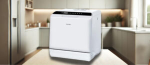 A featured image of the topic ‎Hermitlux HMX-TDJ04 Dishwasher Review. White Hermitlux HMX-TDJ04 countertop dishwasher placed on a light-colored wooden counter in a contemporary kitchen. The unit features a sleek design with a black control panel on top and minimal branding on the front, blending well with the modern surroundings.