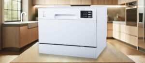 Feature image of SPT SD-2225DWA Dishwasher Review: White SPT SD-2225DWA countertop dishwasher placed on a wooden table in a modern kitchen with light wood cabinets and a window in the background.