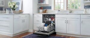 A bright kitchen with white cabinets and a farmhouse sink is complemented by a modern, open built-in dishwasher packed with dishes. The dishwasher's sleek design integrates smoothly with the cabinetry, matching the clean, minimalist aesthetic of the space. Perfect for those researching built-in dishwasher reviews for a home upgrade.