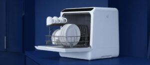 White dishwasher placed on a blue kitchen counter with clean plates and cups inside, showcasing one of the most reliable countertop dishwashers.
