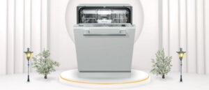 A featured image of the topic Miele G5051SCVi 24 inch Dishwasher Review. A Miele G5051SCVi (24"inches) dishwasher is showcased on a pedestal with a glowing halo at the base, flanked by ornamental plants and other things, set against a backdrop of elegant white curtains.