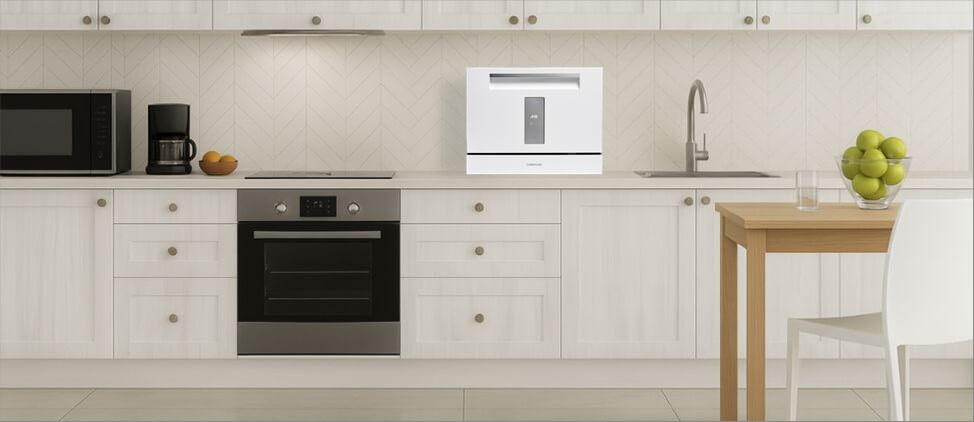 Farberware FCD06SDWHT Size Comparison with Kitchen Setup: A size comparison image of the Farberware FCD06SDWHT dishwasher, illustrating how it fits on a kitchen countertop next to cabinets, a faucet, and average-height individuals.