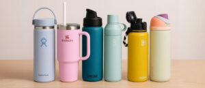 Lineup of the Best Dishwasher Safe Water Bottles including Hydro Flask, Stanley, CamelBak, Ocean Bottle, Fanhaw, and Owala models, displayed on a wooden surface.