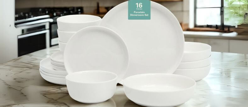 Gibson Home Oslo 16-piece porcelain dinnerware set arranged on a marble countertop in a modern kitchen, showcasing clean white plates and bowls that are dishwasher-safe.