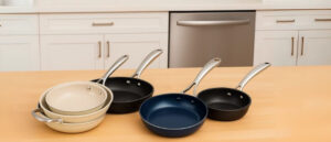 Best dishwasher safe nonstick pans arranged on a wooden kitchen countertop, featuring beige, navy, and black designs with stainless steel handles and a modern dishwasher background.