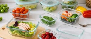 A neatly arranged assortment of dishwasher-safe glass containers on a kitchen counter, featuring a variety of fresh foods like cherries, salad, and vegetables, with some containers left empty for visual contrast.