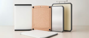 A neatly arranged set of four dishwasher safe cutting boards displayed on a bright countertop, including a white board with black edges, a tan board with non-slip corners and juice groove, a white board with gray edges, and a double-sided stainless steel and plastic board with handles, showcasing various styles and features ideal for mess-free kitchen prep.