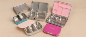 A collection of colorful stainless steel lunchboxes for kids displayed on a wooden surface, showcasing various compartment designs and dishwasher-safe builds.