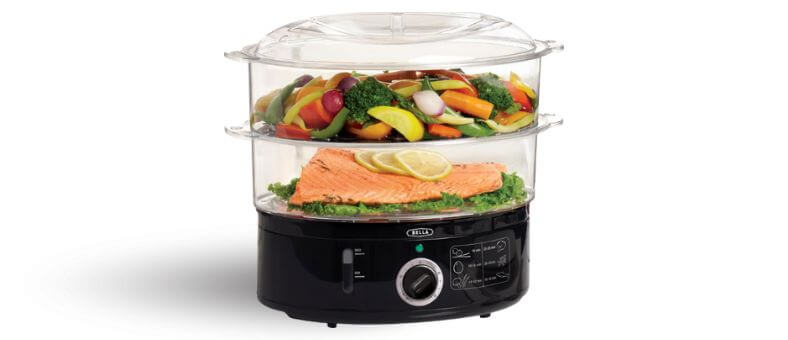 Image shows a two-tier plastic food steamer with steamed vegetables and salmon inside, sitting on a black electric base.