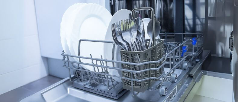 Open dishwasher with a neatly organized cutlery basket in the lower rack, containing forks, spoons, and knives upright beside stacked white plates for optimal cleaning and placement