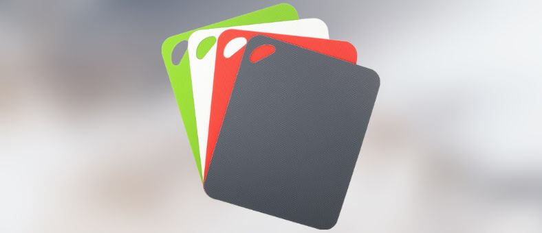 A set of colorful, flexible cutting mats in red, green, white, and charcoal gray, stacked with grip handles for easy use.