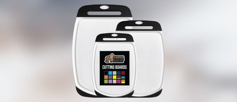 A trio of sturdy, reversible cutting boards with black handles and grips, featuring a centered brand logo and multi-color icons.