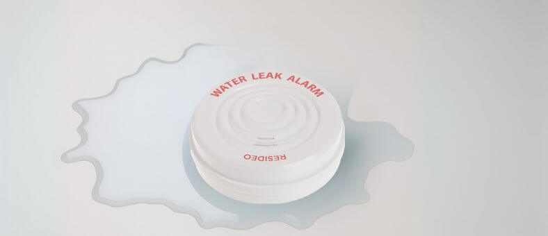 Round Resideo water leak alarm sitting in a large water puddle on a smooth surface.