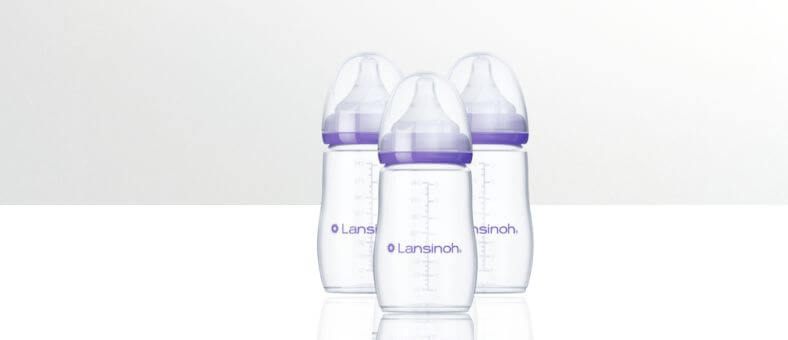 Lansinoh Anti-Colic Baby Bottles – Three clear baby bottles with purple caps, displayed on a white reflective surface.