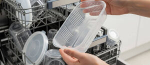 A close-up view of a person holding a damp container above an open dishwasher rack, illustrating Why Plastics Stay Wet in the Dishwasher, as lightweight plastic items retain moisture and dry less effectively compared to glass or metal.