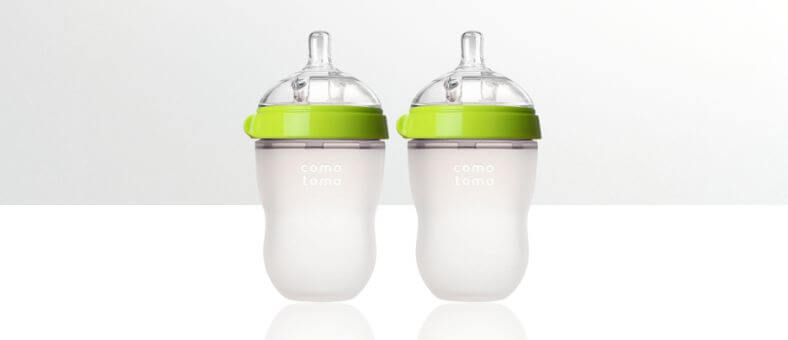 Comotomo Baby Bottles – Two frosted silicone baby bottles with green caps, placed on a white reflective surface.
