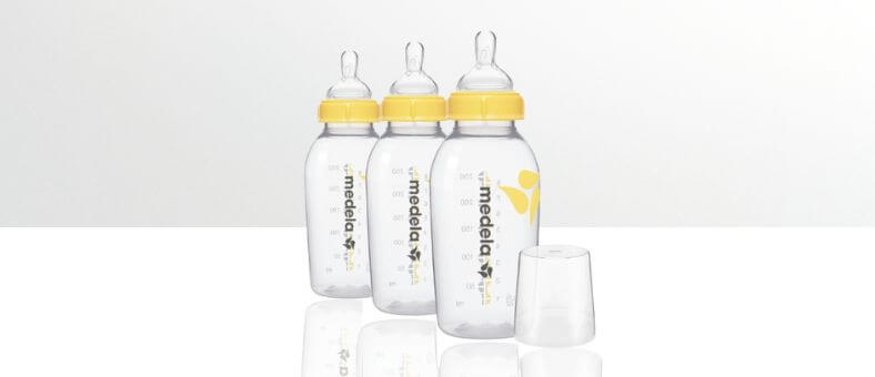 Medela Breastmilk Bottle Set – Three clear baby bottles with yellow caps and silicone nipples, displayed on a white reflective surface with one bottle cap removed.