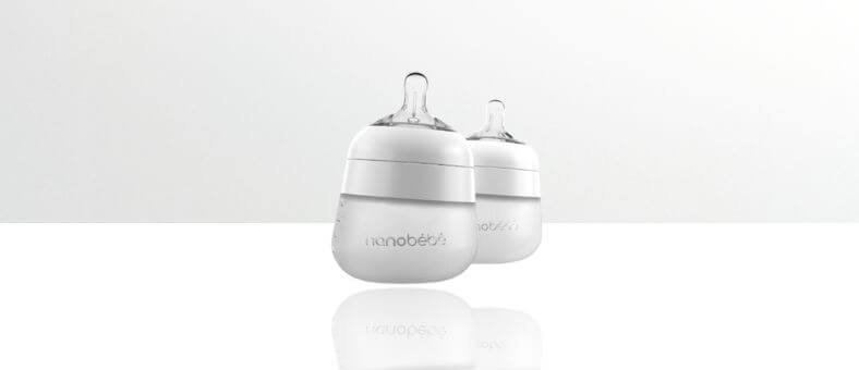 Nanobebe Flexy Silicone Baby Bottles – Two white silicone baby bottles with wide bases and transparent nipples, placed on a white reflective surface.