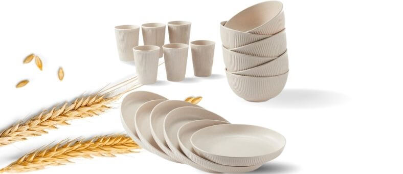 Beige dishwasher safe bamboo dinnerware set with plates, bowls, and cups arranged with wheat stalks for a natural look.