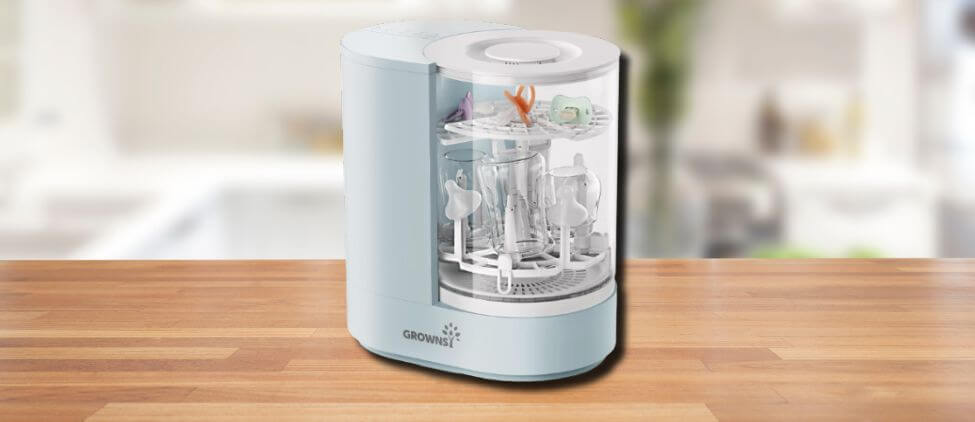 The GROWNSY DeepClean Baby Bottle Washer displayed on a wooden kitchen counter, showcasing its sleek design and clear lid filled with bottles and accessories.