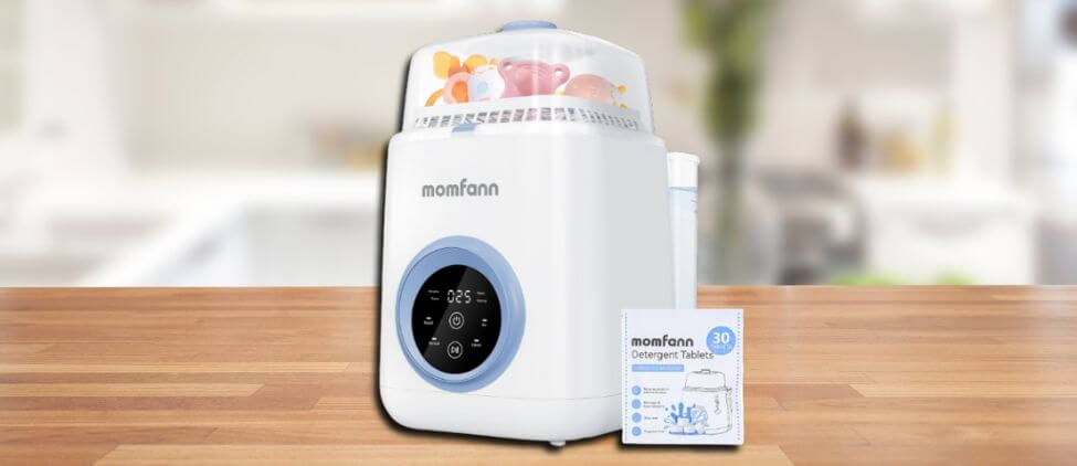 In this Momfann Baby Bottle Washer Review image, the washer is placed on a wooden kitchen counter with detergent tablets beside it, showcasing its modern look and practical everyday placement.