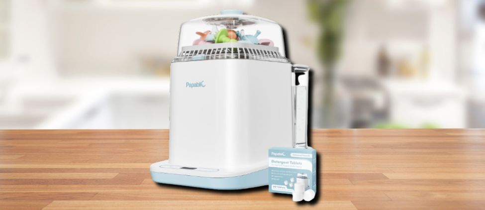 Papablic Baby Bottle Washer placed on a wooden kitchen counter, with detergent tablets and accessories beside it.