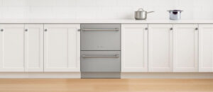 A clean, modern kitchen setup featuring the Fisher & Paykel DD24DV2T9N dishwasher centered between white shaker-style cabinets. The stainless steel Double DishDrawer design blends smoothly with the bright countertop, where two cooking pots rest near the backsplash. This layout highlights the built-in style and premium look of the Fisher & Paykel DD24DV2T9N dishwasher review scene.