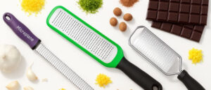 Best Dishwasher Safe Zesters displayed with lemon zest, garlic, chocolate, and spices on a white background.