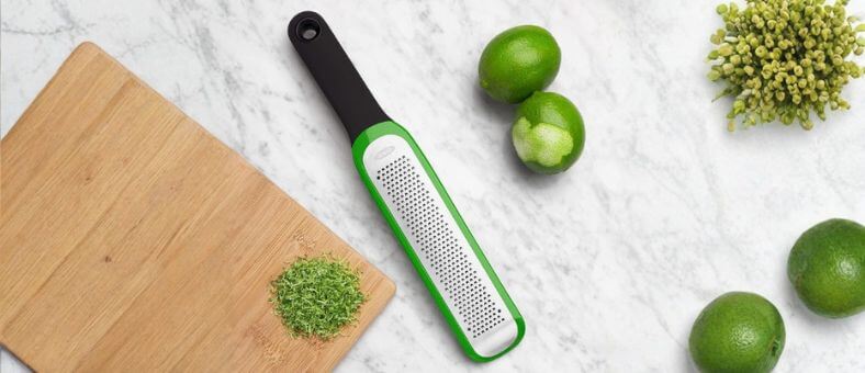 OXO green-frame zester with lime zest on a marble countertop.