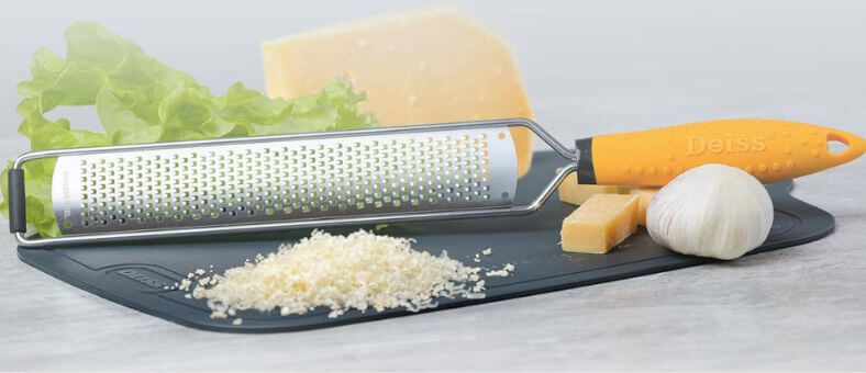 Deiss yellow-handle zester with grated cheese and garlic on a board.